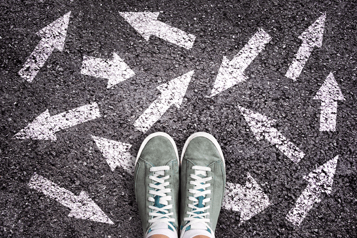 Sneaker shoes and arrows pointing in different directions on asphalt ground
